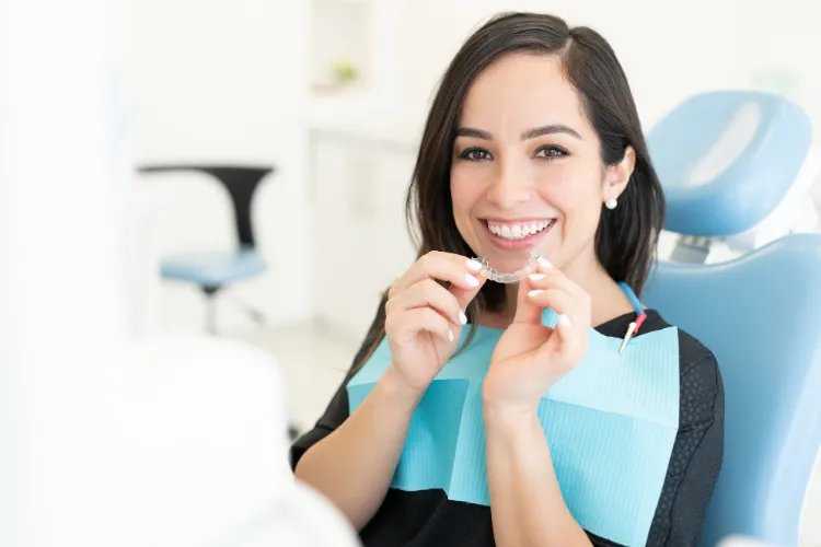 Patient holding clear aligners during a dental visit, highlighting the importance of maintaining oral hygiene and proper aligner care throughout orthodontic treatment.